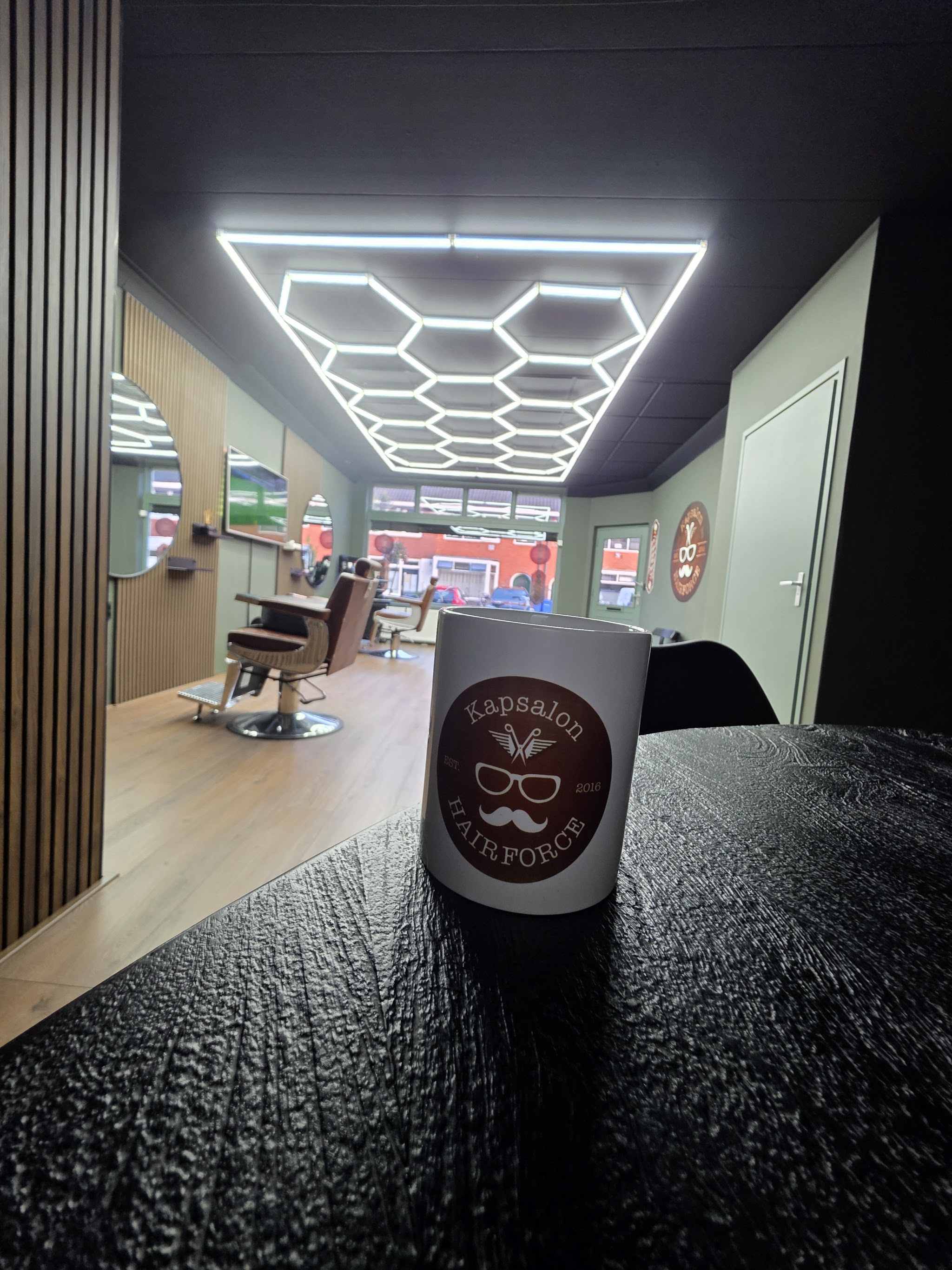 Koffiebeker met het logo van Kapsalon Hairforce op de toonbank